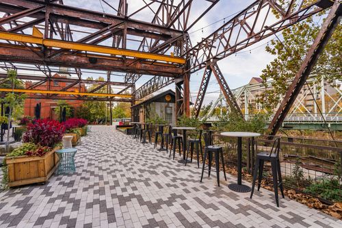 Paver plaza with flower planters and a truss bridge in the distance