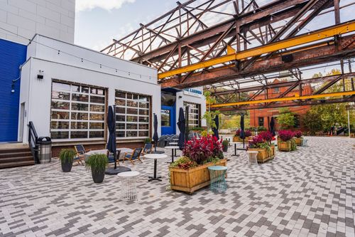 Paver plaza with lounge chairs and flower planters beneath a restored steel trestle