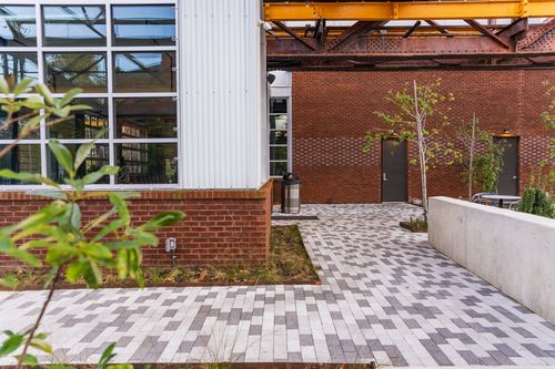Paver walkway along a brick building corner beneath a steel trestle