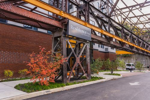 Hotel sign hanging from a steel trestle above a brick facade with fall shrubs