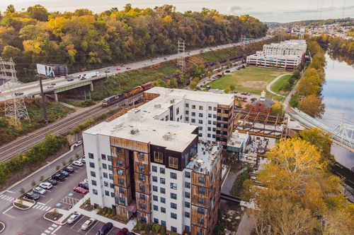Aerial view of hotel construction along a river with a truss bridge and autumn trees