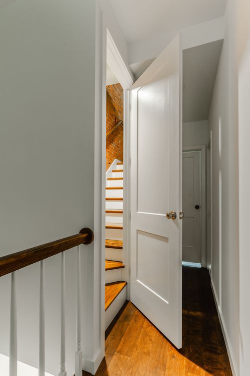 Open white door revealing a narrow staircase to an attic beside exposed brick
