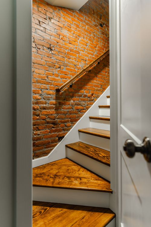 Staircase with white risers, wood treads and an exposed brick accent wall