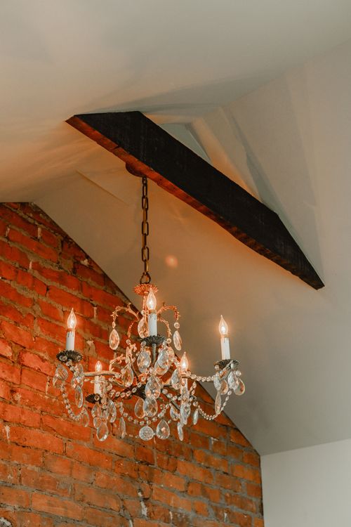 Vaulted peak ceiling with a dark beam and crystal chandelier against exposed brick