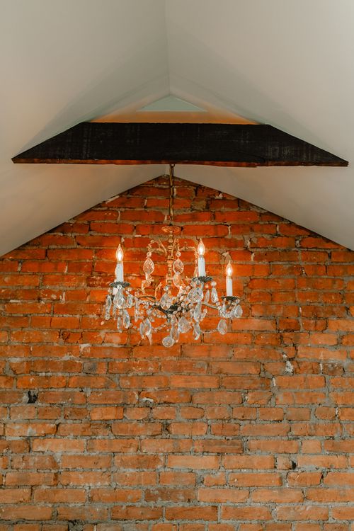 Crystal chandelier centered beneath a vaulted peak with an exposed brick backdrop