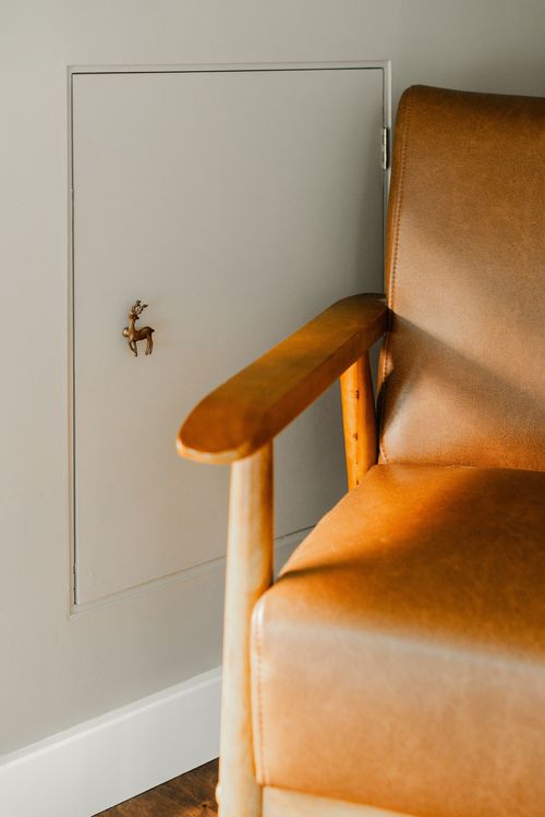 Close-up of a hidden access panel with a tiny brass deer pull beside a leather chair