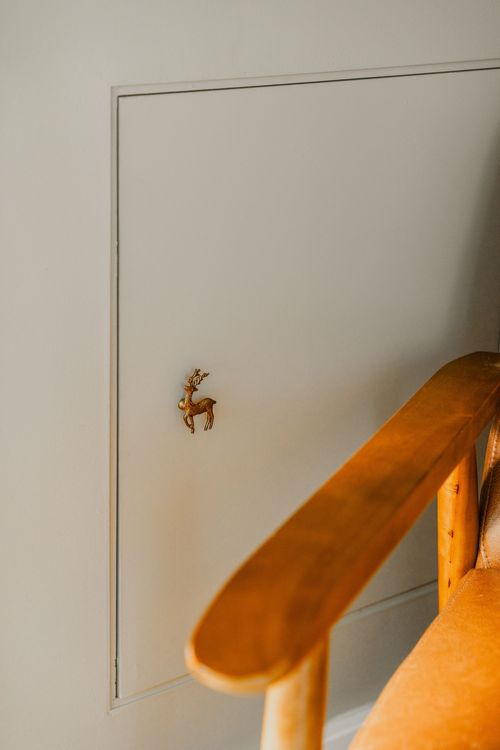 Close-up of a brass deer figurine pull on a wall panel beside a wood chair arm
