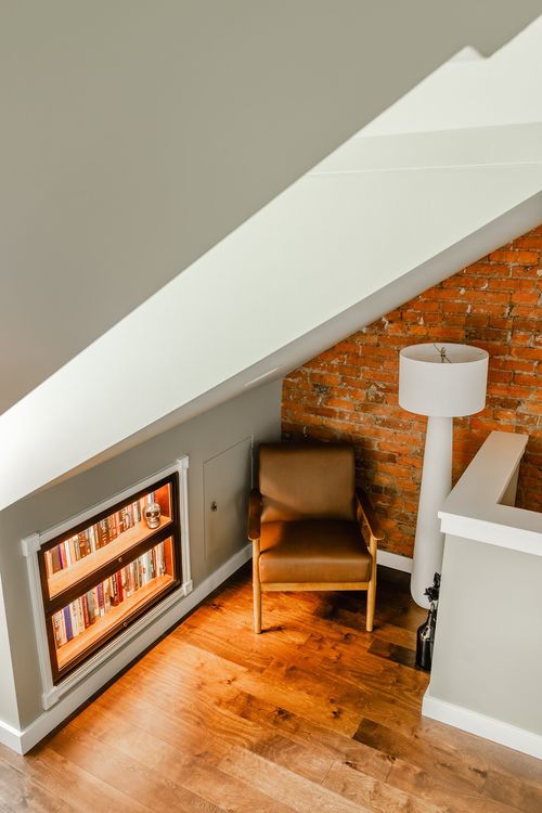Attic reading nook with a lit built-in bookcase and leather armchair under a sloped ceiling