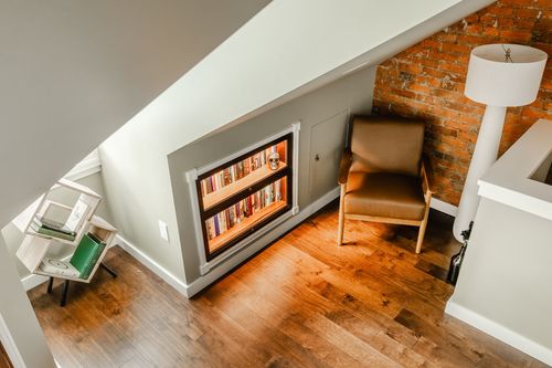 Overhead view of an attic reading nook with a glowing built-in bookcase and leather chair