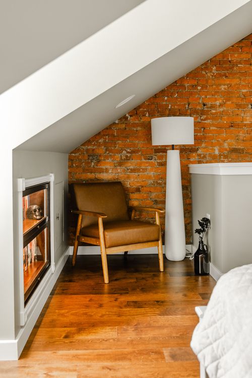 Attic bedroom nook with an exposed brick wall, leather chair and tall white floor lamp