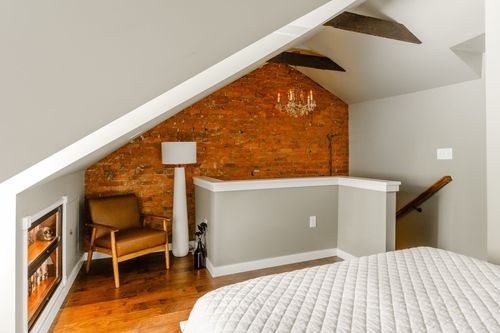 Bedroom with a sloped brick accent wall, chandelier, leather chair and white bedding