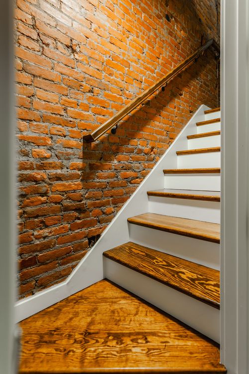 Exposed brick stairwell with a wood handrail and a tiny bronze figurine in a niche