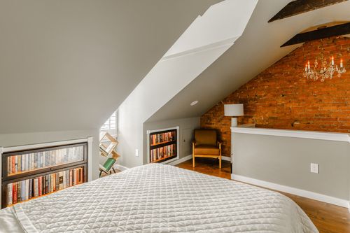 Attic bedroom with lit built-in bookcases flanking the bed and an exposed brick corner