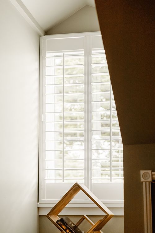 Plantation shutter window beneath a sloped ceiling with a wood book ladder display
