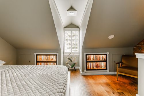 Attic bedroom with symmetrical lit bookcases and a shuttered window