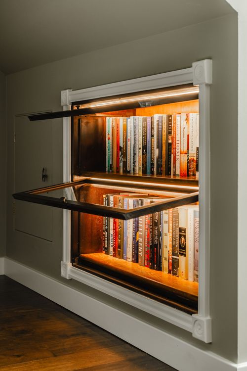 Close-up of an open hidden bookcase door revealing a mirrored, lit interior shelf