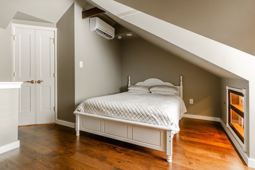 Small bedroom with a white spindle bed, wall-mounted AC unit and beamed ceiling