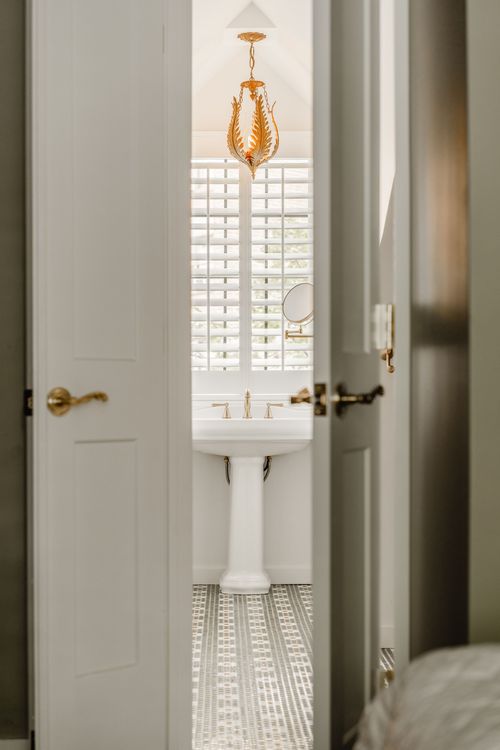 Bathroom doorway framed by a gold pendant light, pedestal sink and penny tile floor