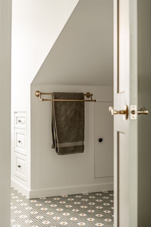 Close-up of a brass towel bar and towel beside white cabinetry and penny tile
