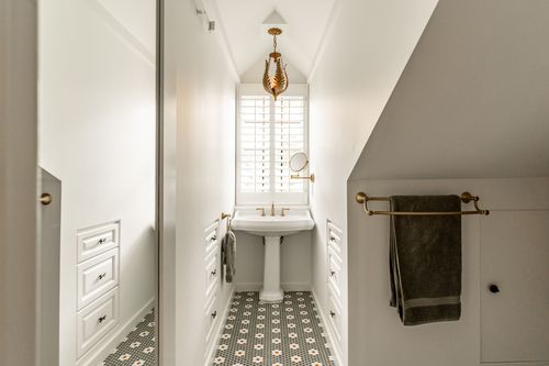 Narrow bathroom with a gold leaf pendant light, pedestal sink and floral penny tile floor