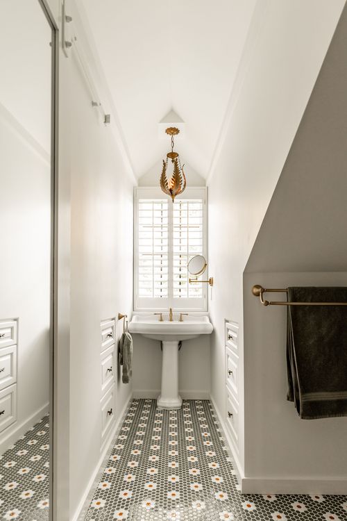 Narrow bathroom with a gold pendant light, pedestal sink, mirror and brass towel bar