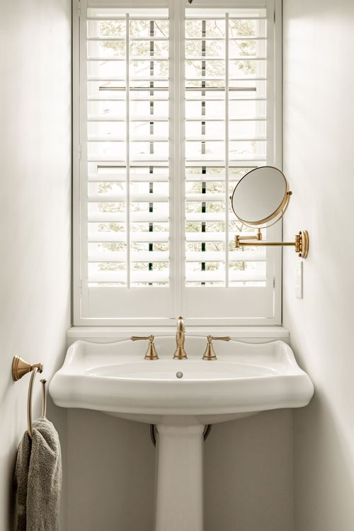 Pedestal sink with a brass gooseneck faucet and a round brass makeup mirror