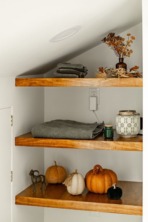 Wood shelves styled with a towel, dried flowers and pumpkins beneath a brass hook