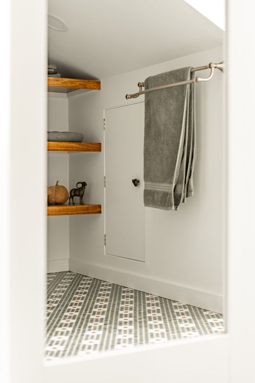 Bathroom door flanked by wood corner shelving and a brass towel bar with a gray towel
