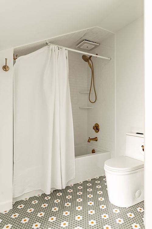 Bathroom shower and tub with a white curtain, brass fixtures and floral penny tile floor