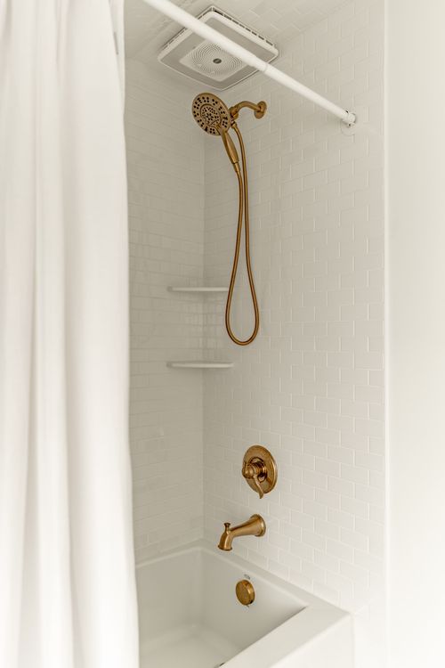 Close-up of a shower alcove with white subway tile and brass handheld shower fixtures