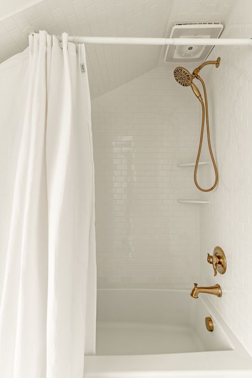 Shower and tub alcove with a sloped ceiling, brass fixtures and white subway tile