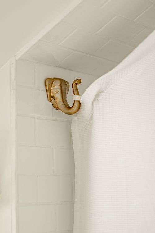 Close-up of a brass elephant-head hook holding a white waffle shower curtain