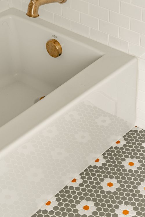 Close-up of a bathtub corner with a brass drain and orange floral penny tile floor
