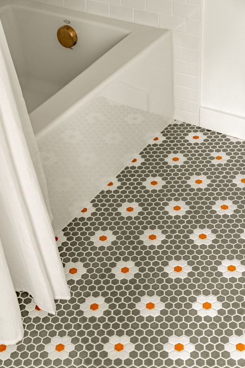 Close-up of a bathtub corner meeting a patterned hexagon penny tile floor