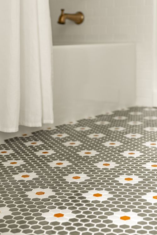 Close-up of a brass tub spout beside a curtain and patterned hex tile floor