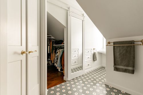 Sliding mirrored barn door open to a walk-in closet with hanging clothes