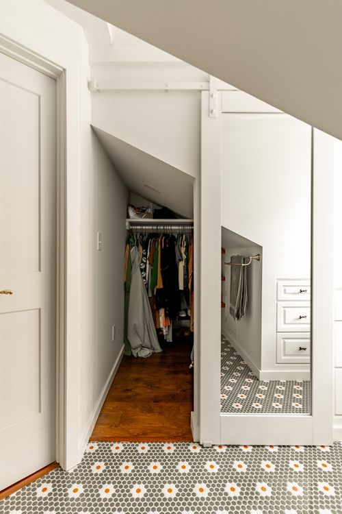 Sloped-ceiling closet nook with hanging clothes and a mirrored sliding door