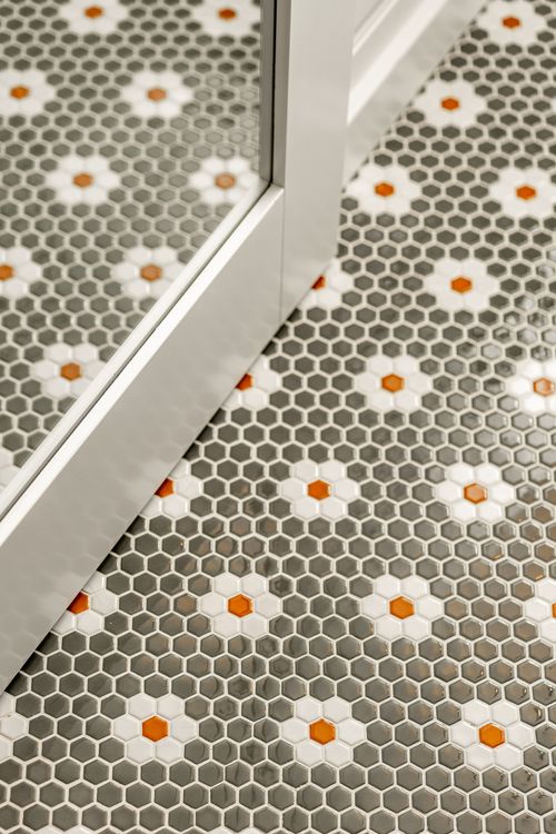 Close-up of a mirrored door frame meeting a hexagon penny tile floor with orange accents