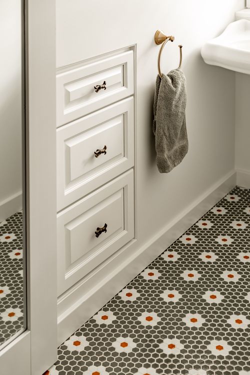 Bathroom vanity drawers with brass ring pulls and a towel beside a hexagon tile floor