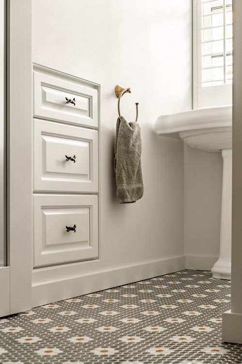 Built-in drawer stack with a towel ring, pedestal sink and shuttered window over hex tile