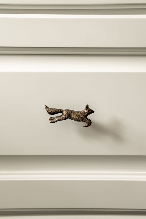 Close-up of a bronze fox-shaped drawer pull on a cabinet front