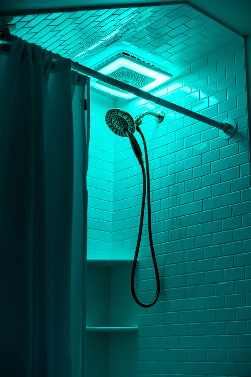 Shower stall lit in teal mood lighting with white subway tile and a brass shower head