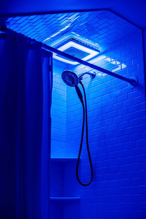 Walk-in shower with white subway tile lit in vivid blue color-changing LED light