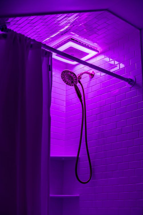 Same walk-in shower washed in purple LED light with a multi-function showerhead