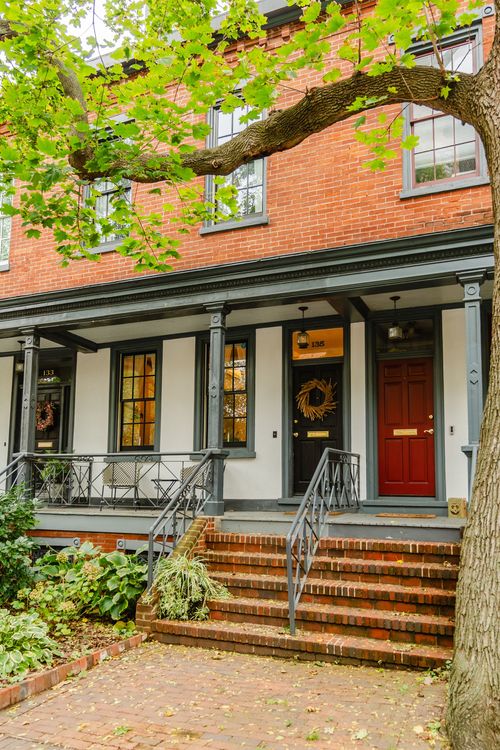 Brick rowhome facade with a red front door, covered porch and wrought iron railings