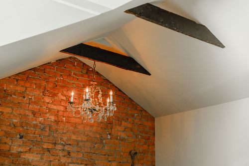 Close-up of a crystal chandelier hanging beneath a dark wood beam against brick