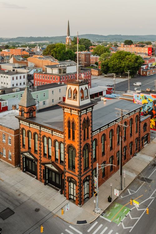 Aerial close-up of an ornate Victorian brick tower with arched windows beside a colorful mural