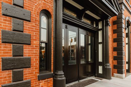 Black-trimmed glass entry doors below gilded lettering on a red brick storefront