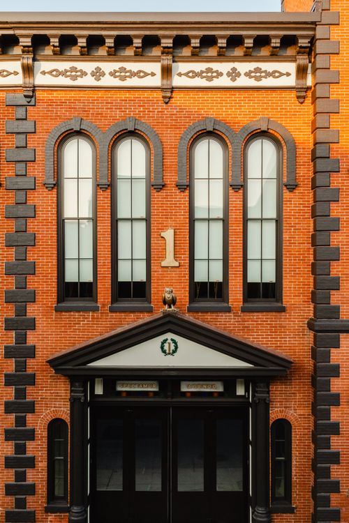 Full brick facade with four arched windows, a bronze owl statue and a gold number 1 above the door