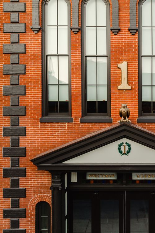 Close-up of arched windows and a bronze owl figure perched above a pedimented entrance